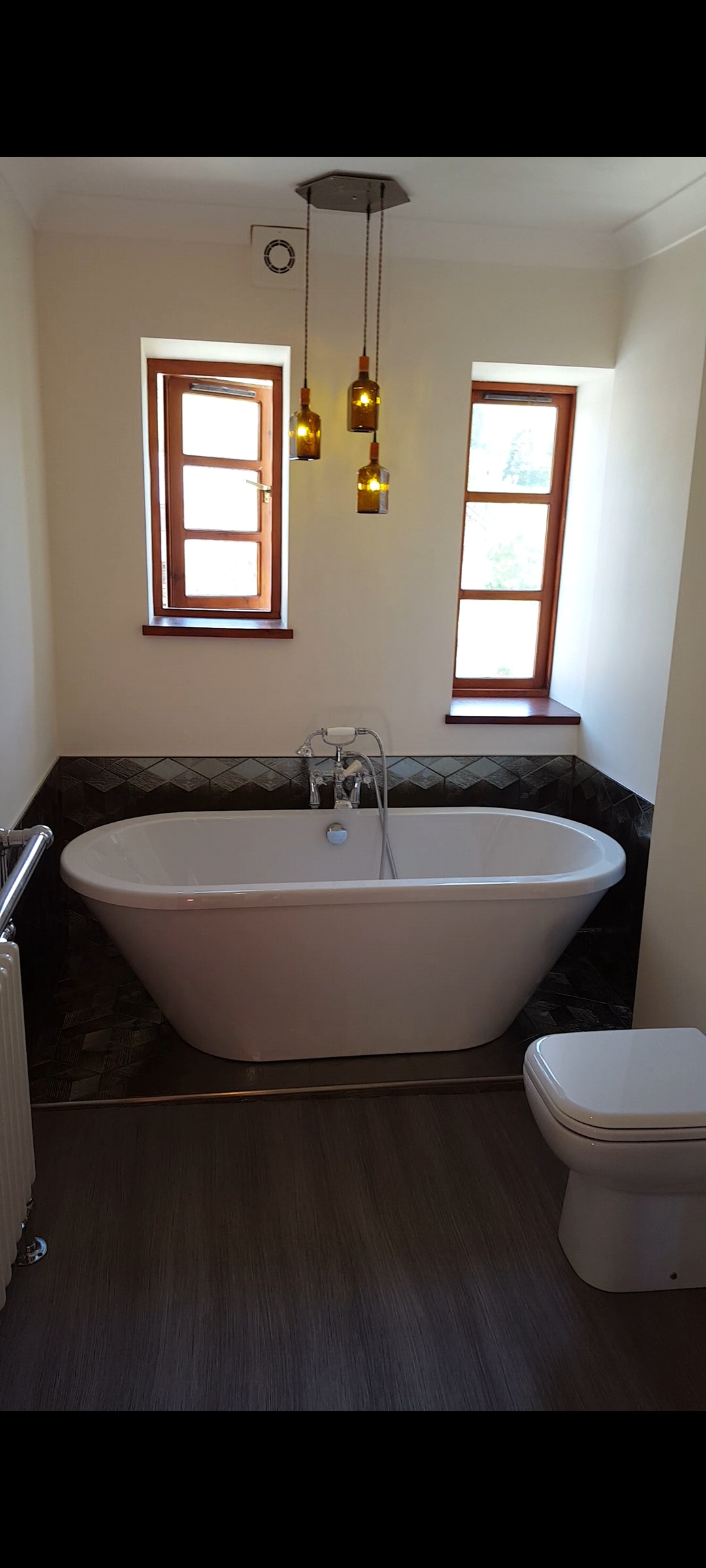 High-end luxury bathroom in Exeter with gold textured tiles, freestanding bath, and back-to-wall toilet with concealed cistern by SBR Property Services Ltd.