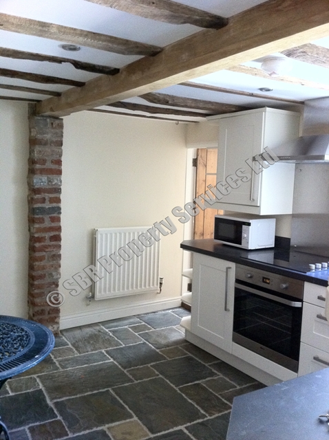 Beautiful made-to-measure cream shaker kitchen in a listed Exeter property with natural slate flooring, exposed brick, a large oak beam, and renovated country doors by SBR Property Services Ltd.