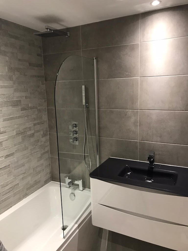 Stylish grey en-suite bathroom in Exeter with a large black wall-hung basin, bath with shower screen, and concealed thermostatic shower valve by SBR Property