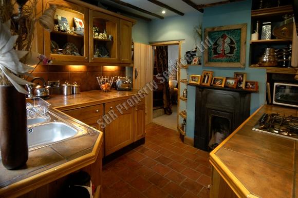 Beautiful hand-built oak kitchen in an Exeter listed building with restored quarry tiles, exposed beams, and a reclaimed cast iron fireplace by SBR Property Services Ltd.