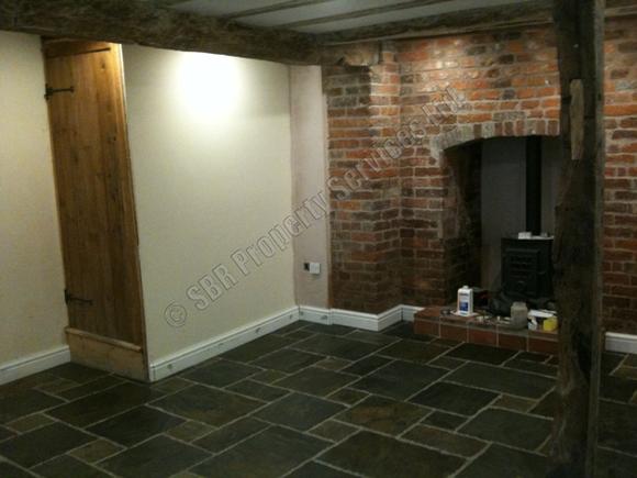 Beautifully renovated lounge in a listed Exeter building featuring natural slate tile flooring, exposed supporting beams, and exposed brick by SBR Property Services Ltd.