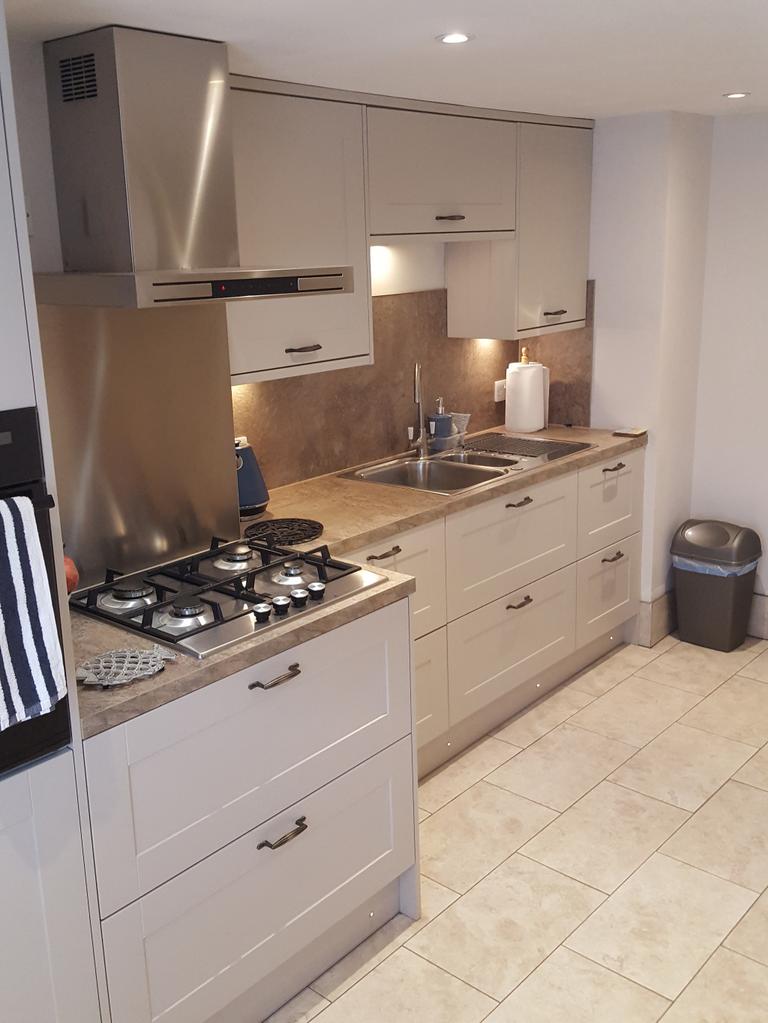 Stylish cashmere shaker kitchen in Exeter with stone worktops, realistic limestone floor tiles, and under-cabinet lighting by SBR Property Services Ltd.